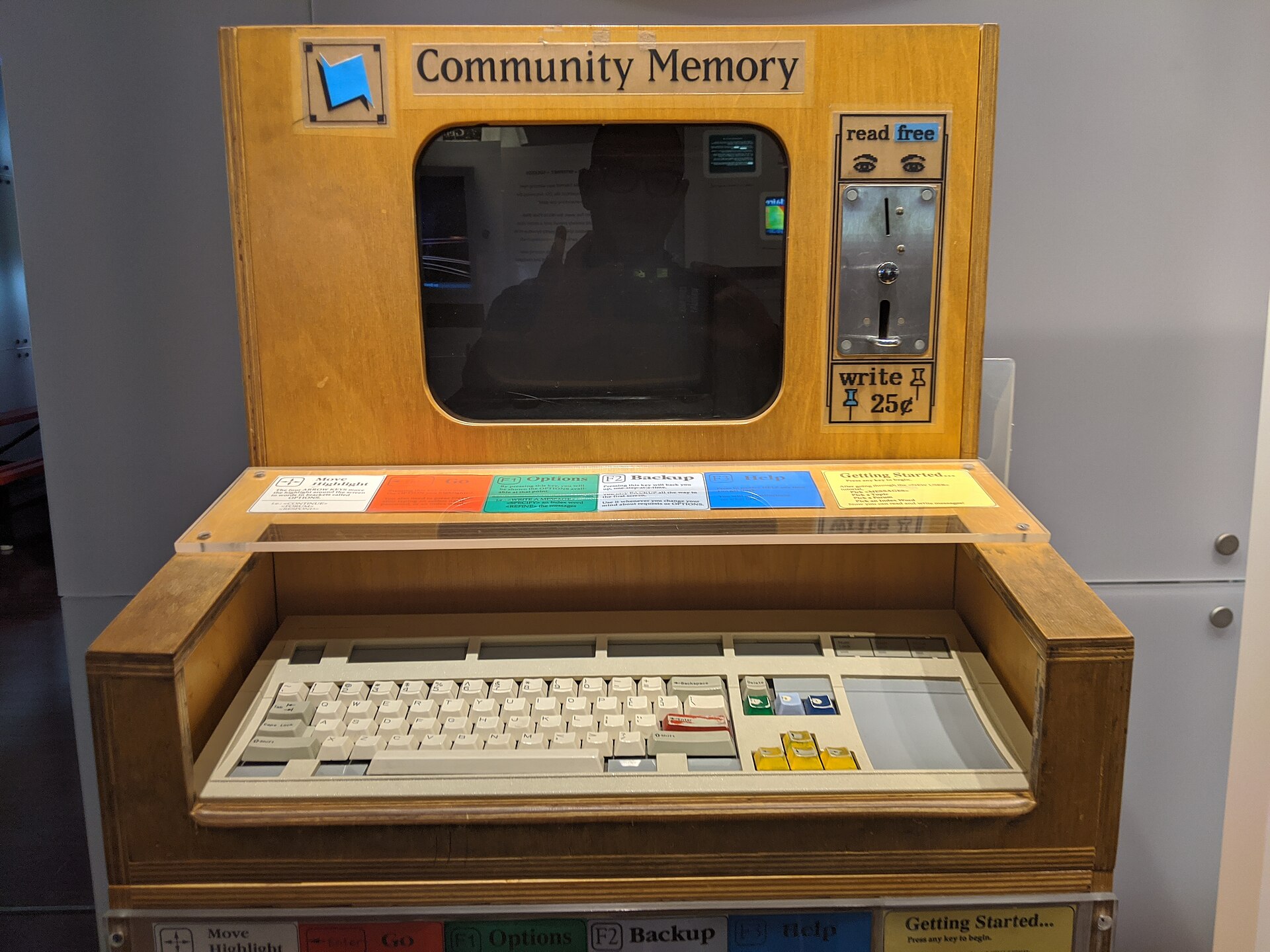 A wooden Community Memory public computer workstation with a screen, keyboard, and coin slot.
