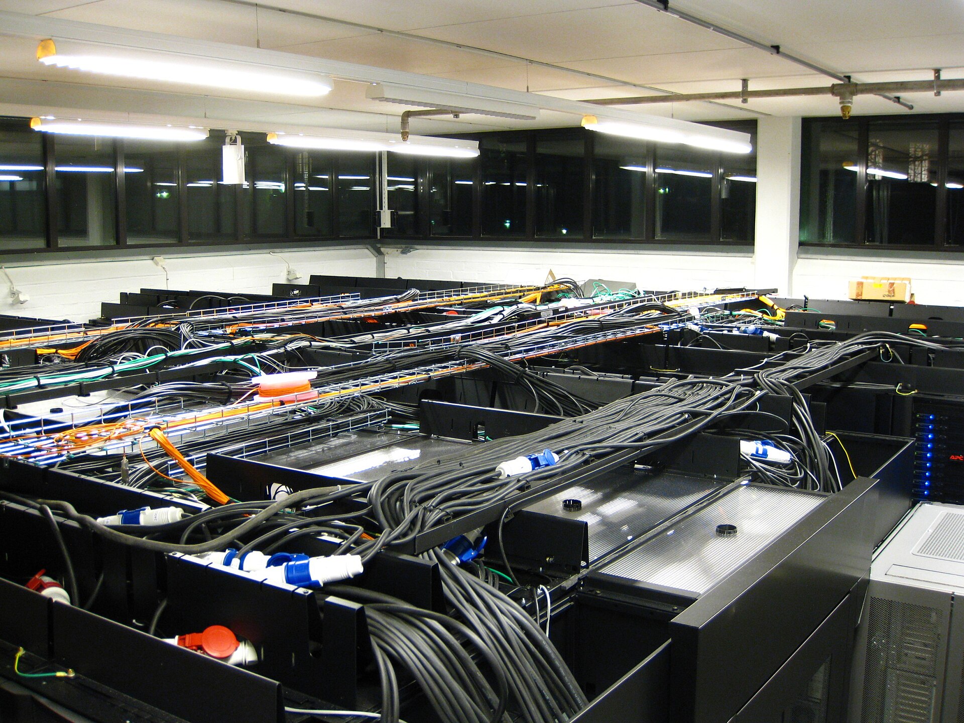 Dense rows of servers, power cables, fiber-optic lines, and network infrastructure in a parallel computing center.